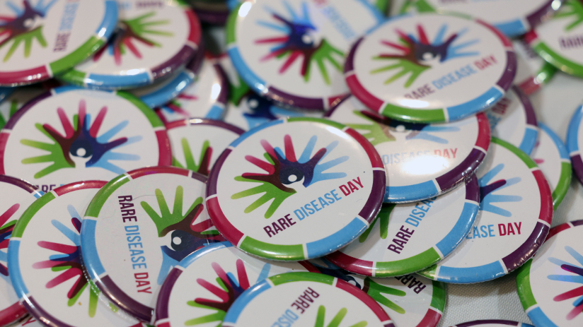A pile of round badges for Rare Disease Day. The Rare Disease Logo is in the centre with the branded colours in segmented around the edge.