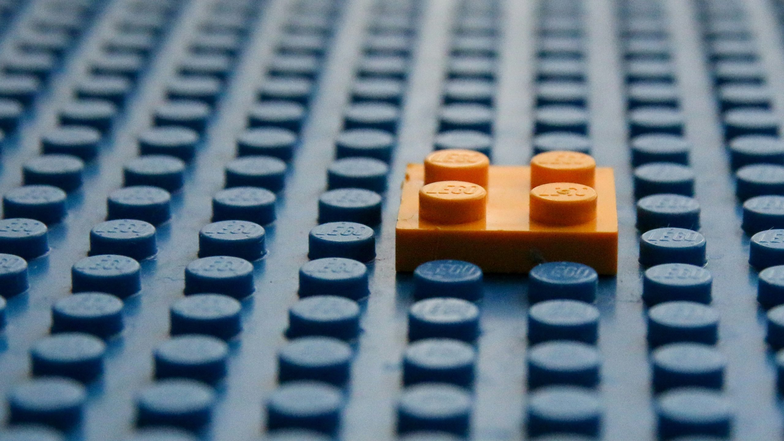 A small orange square lego brick attached to to a large grey lego sheet