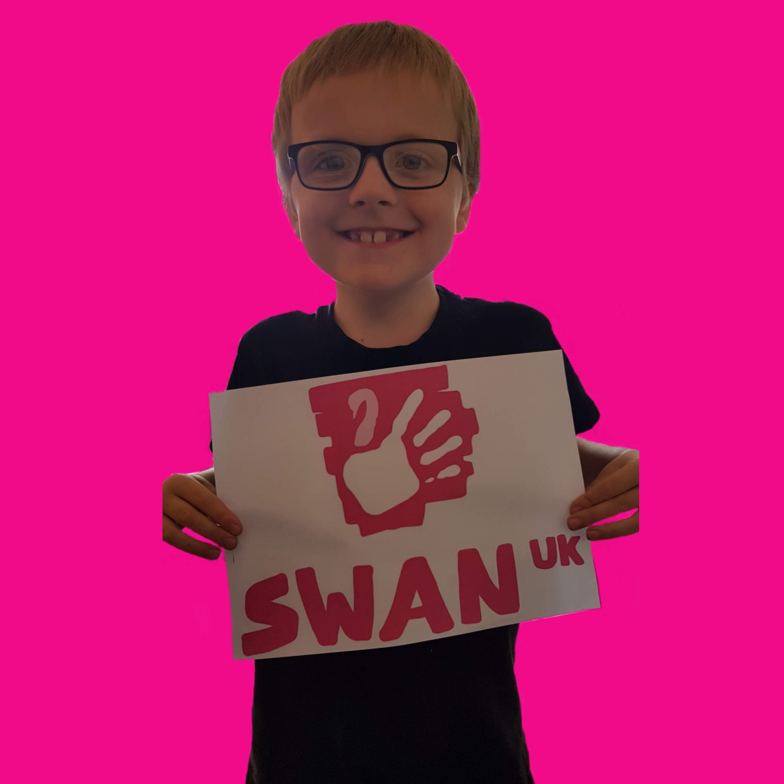 A young boy with glasses holds up a SWAN UK sign. He is cropped onto a bright pink background