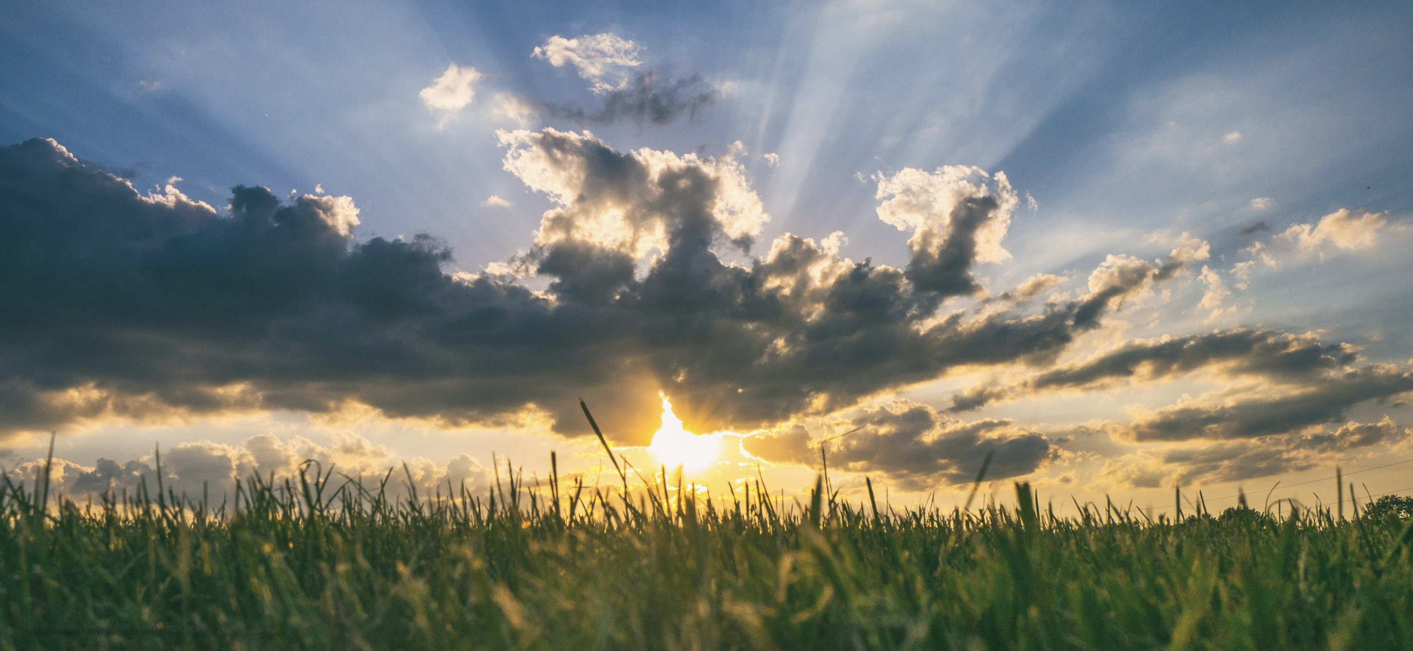 A sunshine peeking out the clouds over a field.