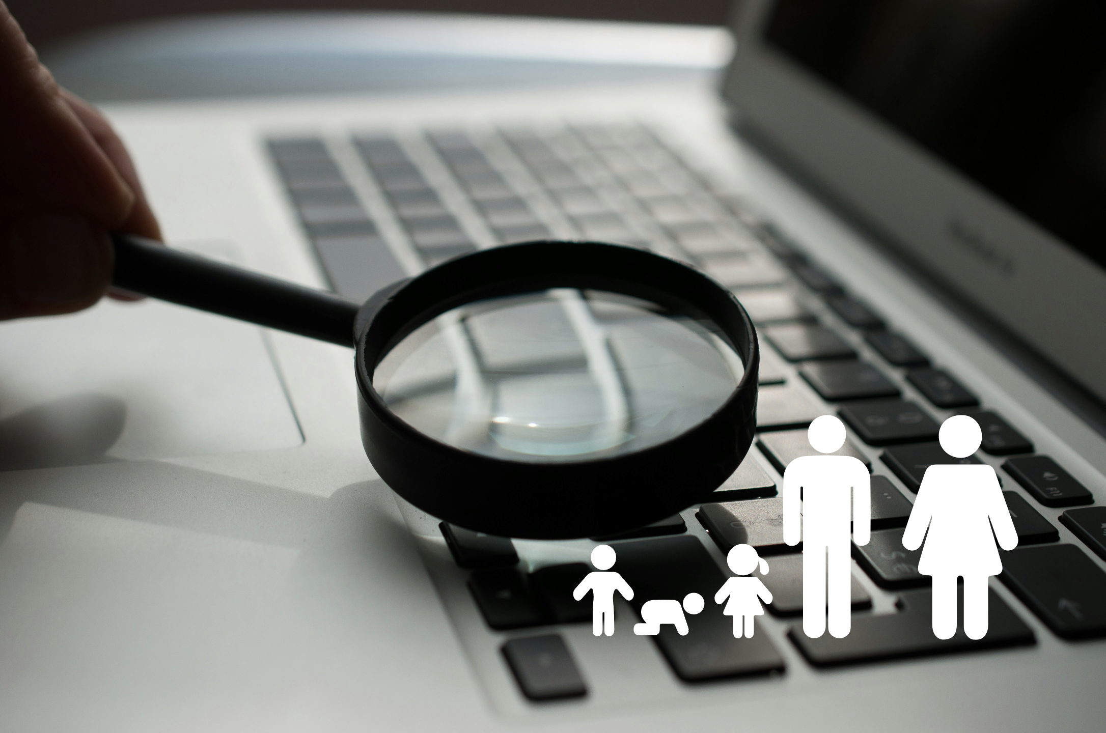 magnifying glass on a laptop keyboard. Two adult and three children icons are in the corner of the image