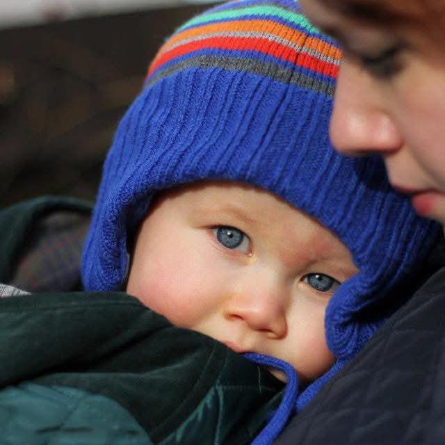 A headshot of a toddler wearing a wooly hat and coat with his head against his mum's shoulder.